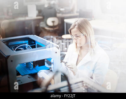 Female technician, 25-30 years, in white lab coat and goggles, controlling printing of a 3D printer, Wattens, Innsbruck Land Stock Photo