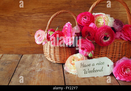 pink flowers in the basket next to card with phrase: HAVE A NICE WEEKEND, on wooden table Stock Photo