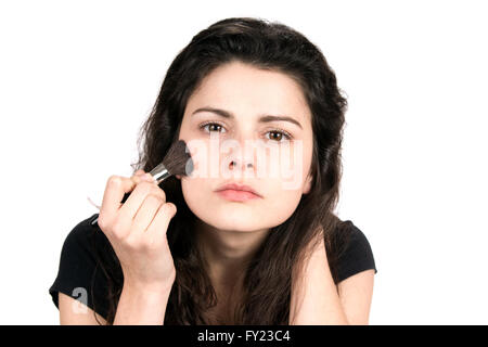 Young woman uses a cosmetic brush to apply blush makeup to her face. Stock Photo