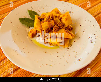 Italian pasta dish on a white plate pappardelle con ragu di cinghiale wild boar olive oil bay leaf Italian food cooking in Italy Stock Photo