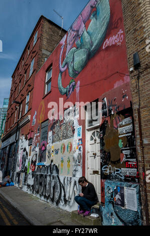 A girl sitting on the doorstep in front of houses full of murals and street art in east london Stock Photo