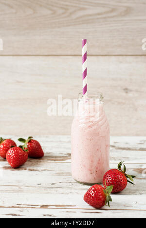 Strawberry milk in glass bottle with straw on old vintage wooden background. Fresh strawberries, light wood table.