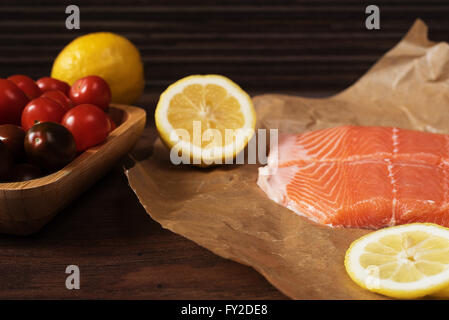 Raw salmon on baking paper, cherry tomatoes, lemon and parsley. Rustic wooden background Stock Photo