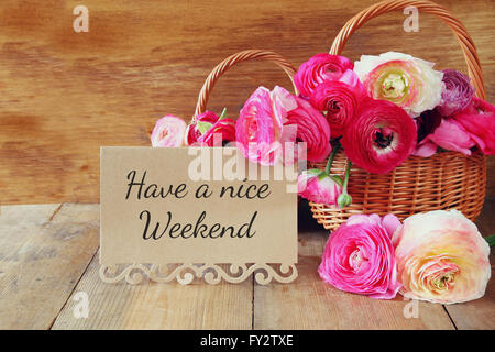 pink flowers in the basket next to card with phrase: HAVE A NICE WEEKEND, on wooden table Stock Photo
