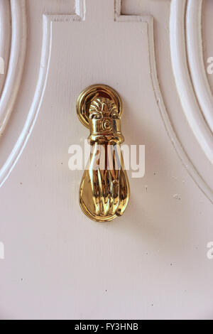 Brass door knocker in form of a hand, on white door Stock Photo