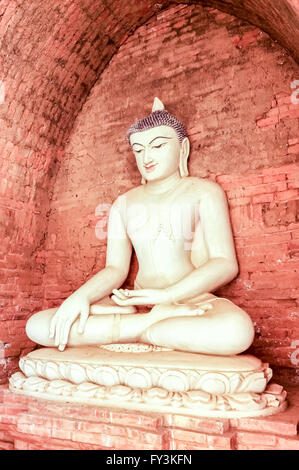 White Buddha burmese style in front of brick stone wall meditating in full lotus posture Stock Photo