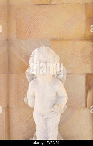 Old Cupid statue with have a backdrop is brown brick wall. Stock Photo