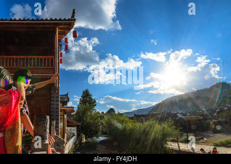 Chinese tourist couple watches the traditional village in front of mountain scenery and the setting sun. Stock Photo