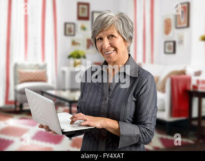 Senior woman using her handheld laptop as she stands in the living room of her house Stock Photo