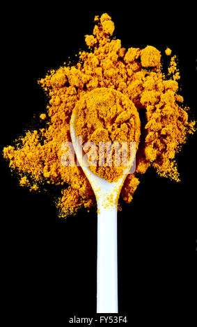 Ground turmeric spice in a white spoon isolated on a black background Stock Photo