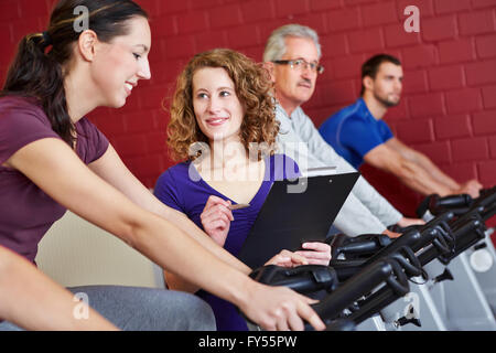 Female fitness trainer helping woman on spinning bike in fitness center Stock Photo
