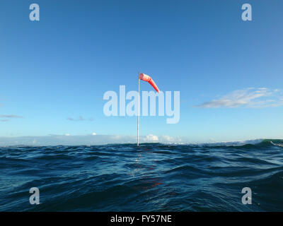 Flag pole with wind sock rises above the wavy waters of Waikiki, Hawaii. Stock Photo
