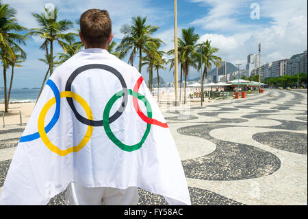 RIO DE JANEIRO - MARCH 10, 2016: Athlete draped in Olympic flag stands in front of the patterned boardwalk at Copacabana Beach. Stock Photo