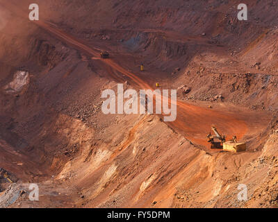 Top view of sunlit open-pit mine with quarry excavator loading iron ore to dump truck Stock Photo