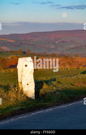 A view from Halkyn Mountain towards Moel-y-Parc in the Clwydian Range hills on the Flintshire side of the range as the moon sets over the skyline and an old road marker visible marking the road in winter weather Stock Photo