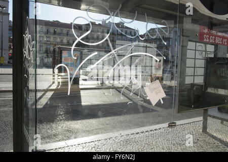 A perspex bus shelter is etched with grafiti. The early morning sun casts long shadows. Stock Photo
