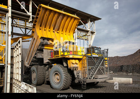 Large dump truck dumping copper ore into giant crusher Stock Photo