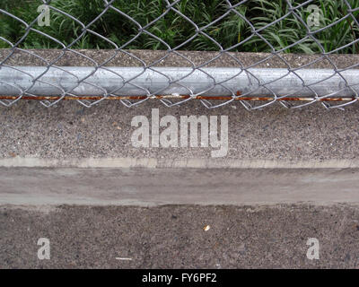 Rusted Chain link fence and concrete sidewalk its attached to and plants below in Costa Rica. Stock Photo
