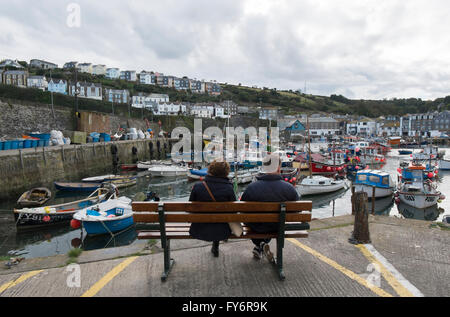 Couple sitting on a bench looking at the harbour at Mevagissey, Cornwall, UK Stock Photo