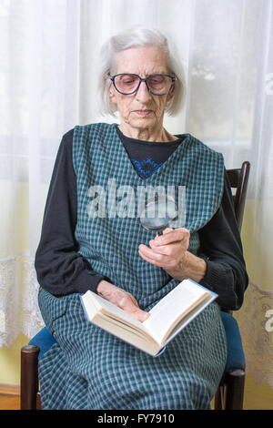 Ninety years old grandma reading a book through magnifying glass Stock Photo