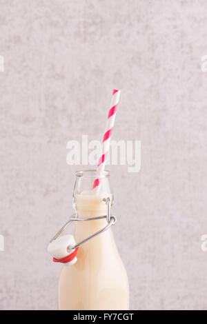 Oat milk in a glass bottle with striped drinking straw in close up. Stock Photo