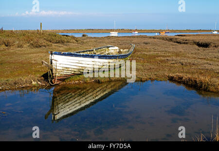 A deserted small clinker built fishing boat on salt marshes at Brancaster Staithe, Norfolk, England, United Kingdom. Stock Photo