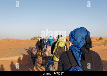 Camel trip in the evening with several people photographed from behind in the Erg Chebbi desert near Merzouga in Morocco.