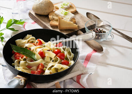 Tagliatelle Pasta with cherry tomatoes in a pan, on white wooden table and red checkered tablecloth