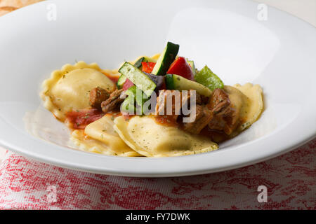 fresh meat tortellini with tomato and sauteed vegetables on red and white tablecloth Stock Photo