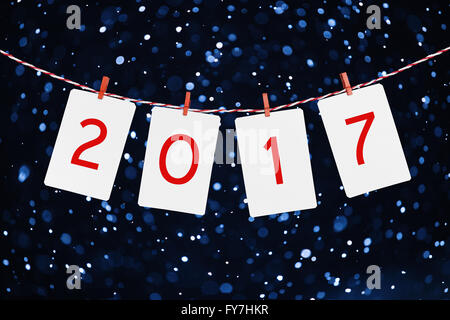 Paper or photo frames  with 2017 figures hanging on the red striped rope. Snowfall background, New year design. Stock Photo