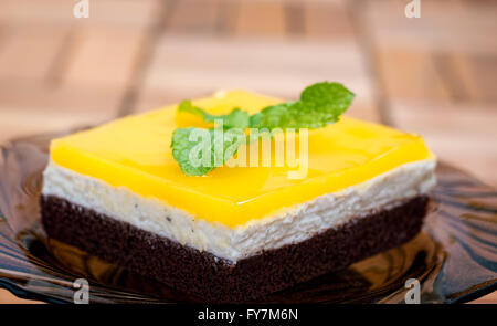 Lateral view of chocolate sponge, cheese cream filling and orange juice jello topping cake decorated with mint leaves. Stock Photo