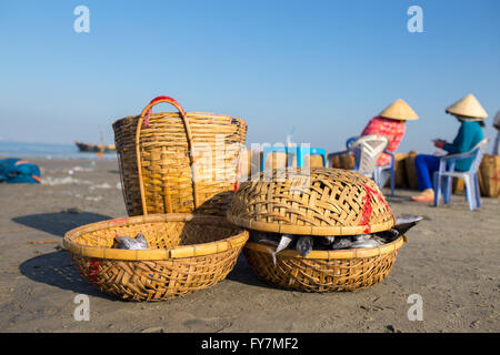 Fishing basket with two woman, wearing conical hat in background under blue sky at Long Hai beach, Ba Ria, Vung Tau, VietNam Stock Photo