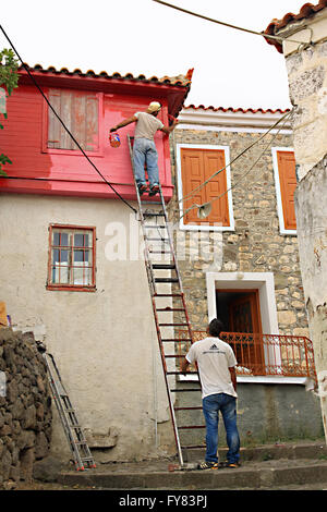 Two men painting a house  one holding the ladder and the other at the top painting Stock Photo