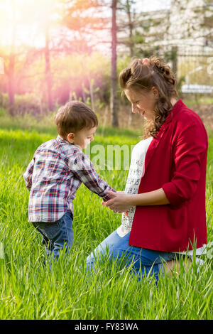 Beautiful pregnant woman outdoor with her happy little boy in the park. Stock Photo