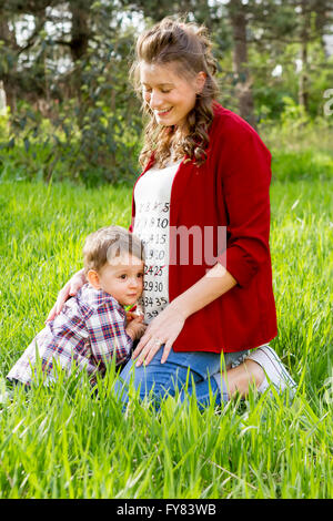 Beautiful happy pregnant woman outdoor with her little boy in the park. Stock Photo