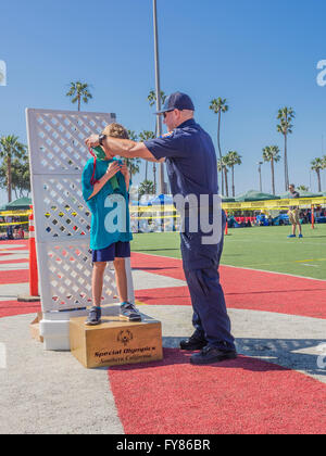 A disabled young boy 10-12 receives his award from a uniformed fireman for competing in the Southern California Special Olympics Stock Photo