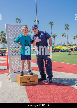 A disabled young boy 10-12 receives his award from a uniformed fireman for competing in the Southern California Special Olympics Stock Photo
