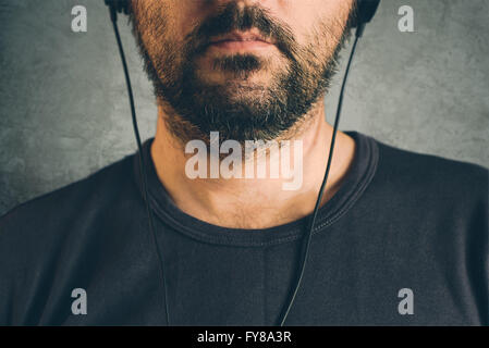 Unshaven adult man listening to music on headphones, enjoy favourite song, half face low key portrait Stock Photo