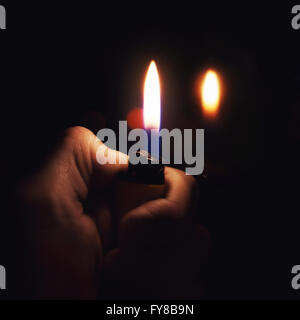 Male hand holding a burning lighter in the dark Stock Photo