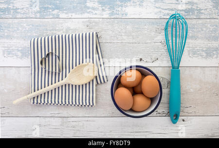 Eggs in a bowl with a whisk wooden spoon and napkin on a rustic wood table top shot from above Stock Photo