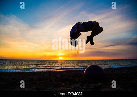 Aberystwyth Wales UK, Saturday 23 April 2016 UK weather: As the sun sets over Cardigan Bay in Aberystwyth at the end of a day of sunshine but cold northerly winds, teenager BILLY ASHTON, on a weekend break from Birmingham, performs acrobatic leaps in the air off the beach. photo Credit:  Keith Morris/Alamy Live News Stock Photo