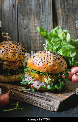 Two Homemade veggie burgers with sweet potato, fresh radish and pea sprouts, served on wooden chopping board over wooden backgro Stock Photo