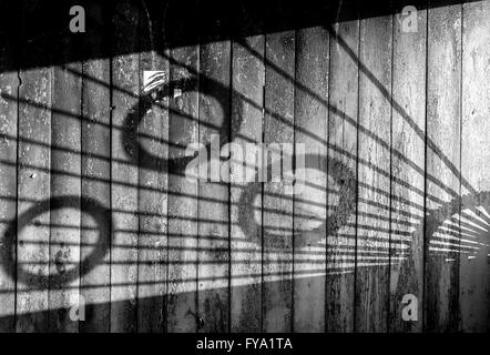 Shadows from a metal patterned bus stop create a light abstract on the aged wood. Black and white monochrome image Stock Photo