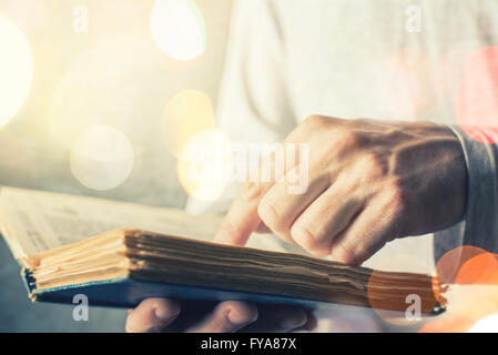 Man reading old book with torn pages, close up of adult male hands holding vintage book, bokeh light in background. Stock Photo