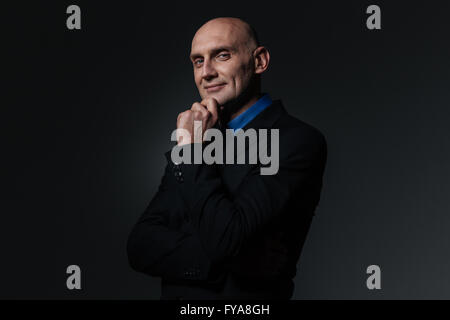 Smiling handsome businessman in suit standing and thinking over black background Stock Photo