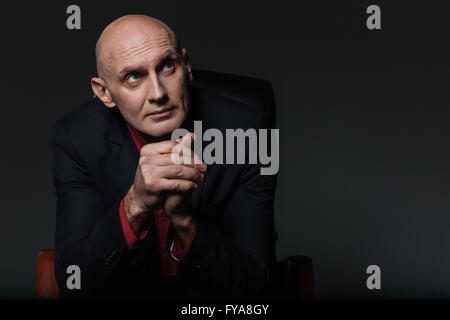 Pensive businessman sitting in office chair and thinking over black background Stock Photo