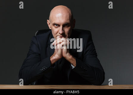 Serious handsome businessman sitting at the table over black background Stock Photo