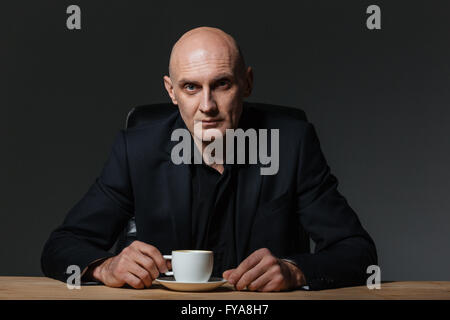 Handsome businessman sitting at the table and drinking coffee over black background Stock Photo