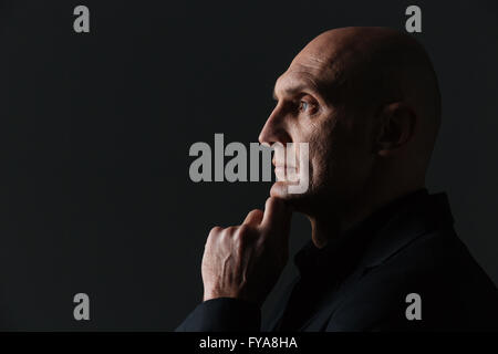 Profile of thoughtful attractive businessman thinking and  touching his chin over black background Stock Photo