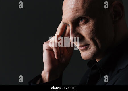 Closeup of pensive attractive businessman touching his temple and thinking over black background Stock Photo